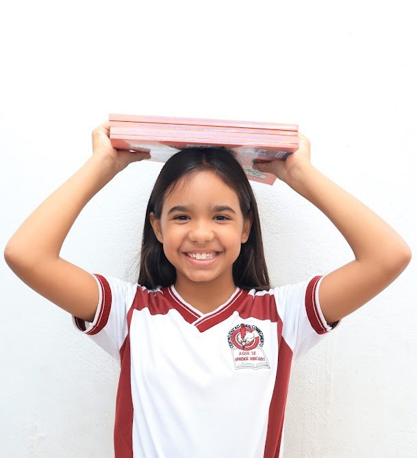 Aluna do Ensino Fundamental sorrindo com livros sobre a cabeça