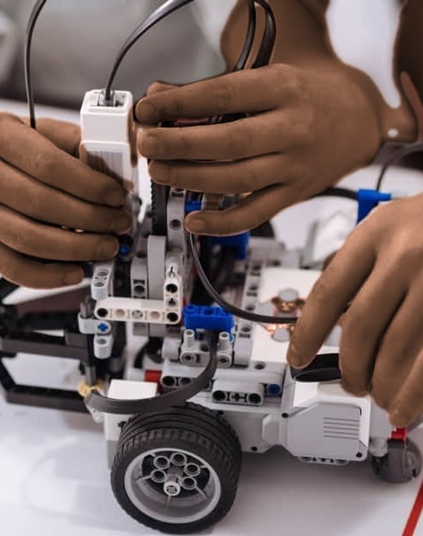 Mãos de alunos montando e programando um robô na aula de Robótica